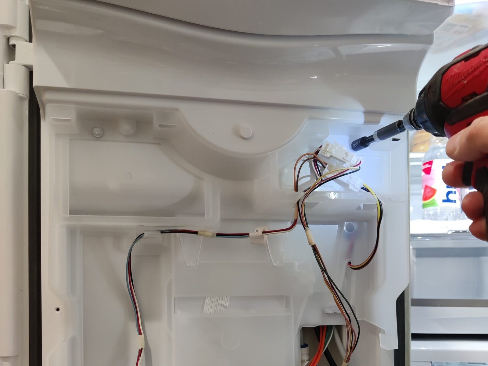 Professional appliance repair technician inspecting internal wiring and electrical components of a Sub-Zero refrigerator.