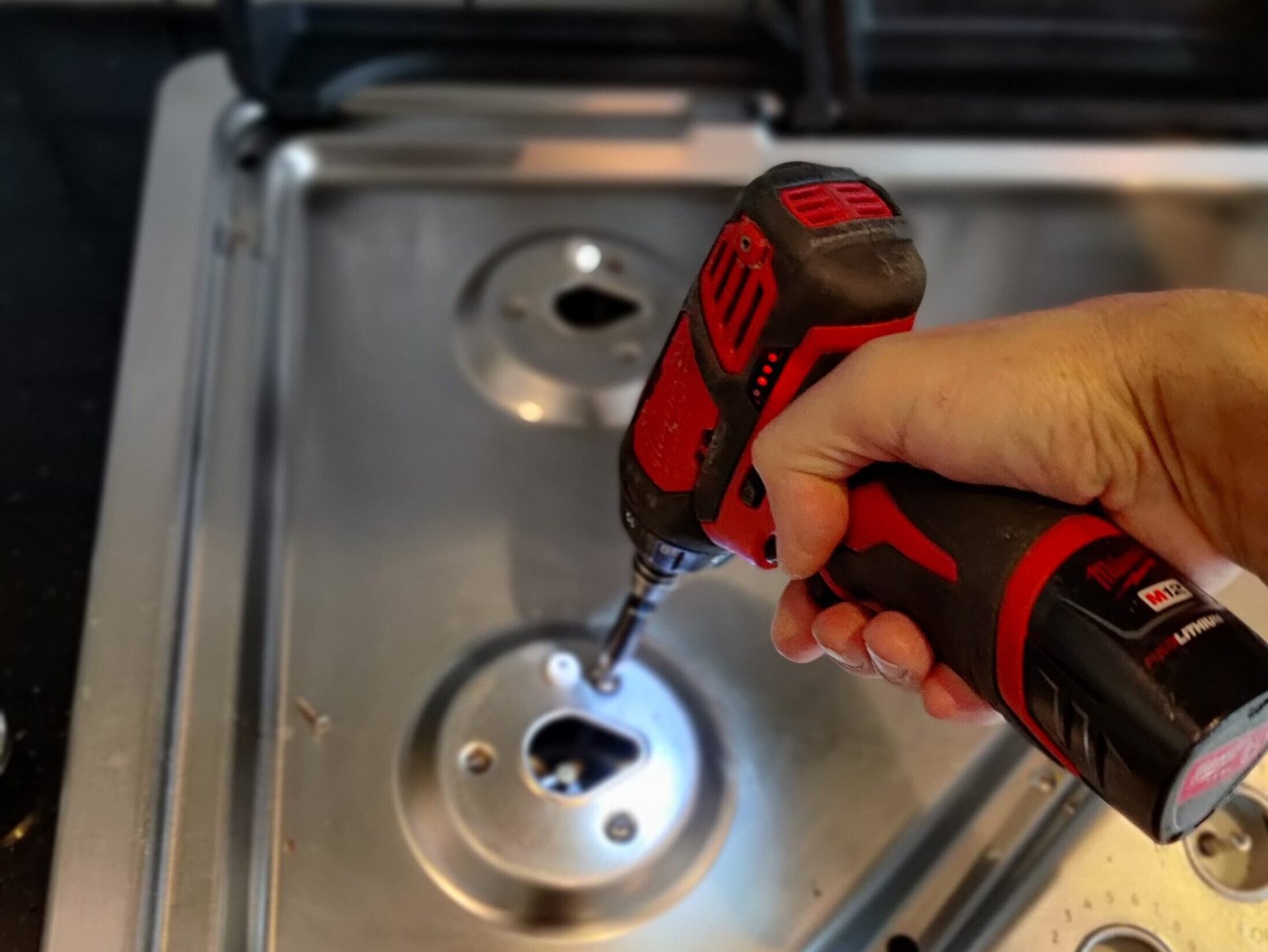 Technician using a cordless power tool to service a high-end Wolf gas cooktop in a residential kitchen.