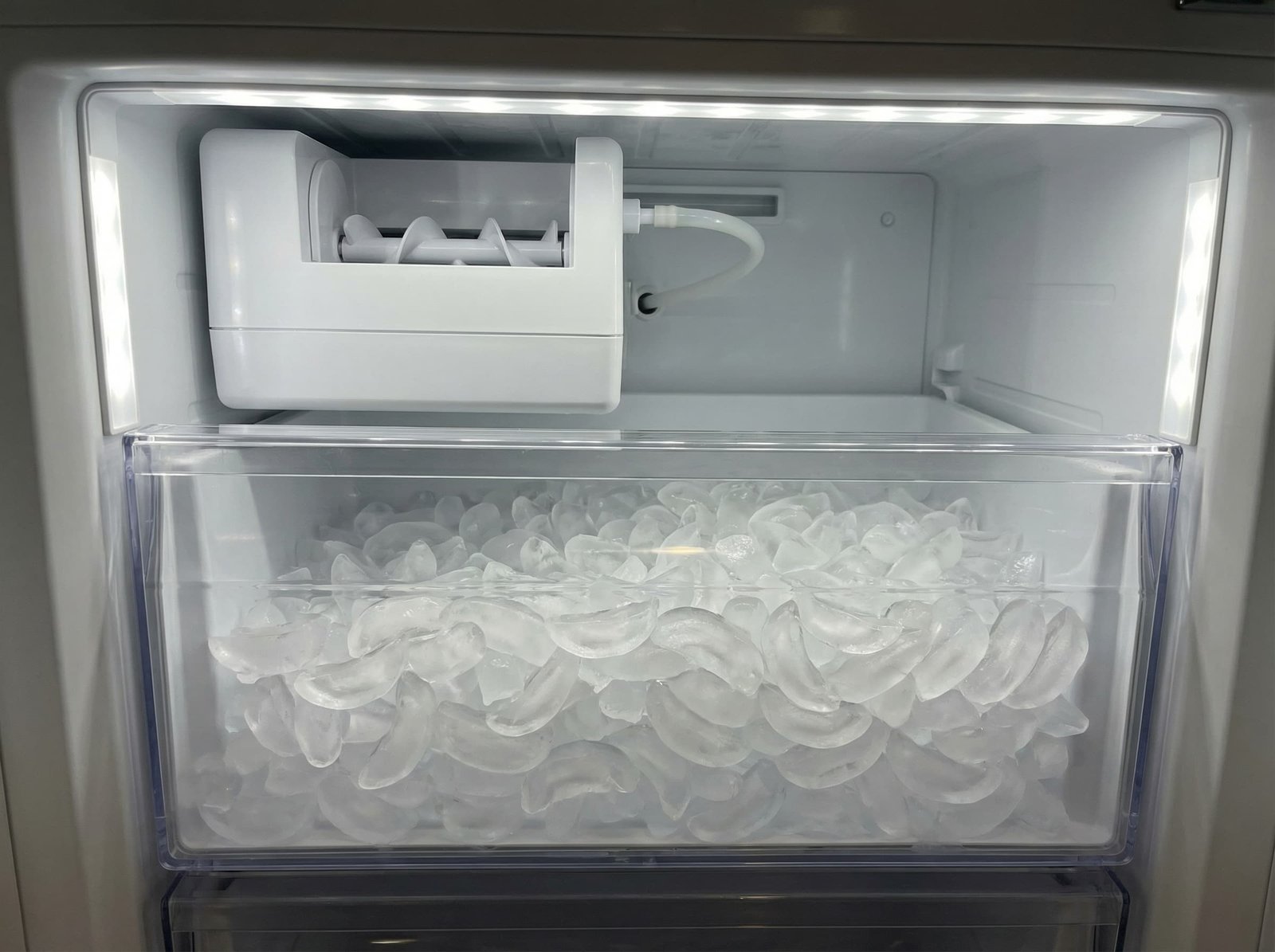 Clean and functional built-in ice maker unit producing crescent-shaped ice cubes in a Sub-Zero refrigerator freezer.