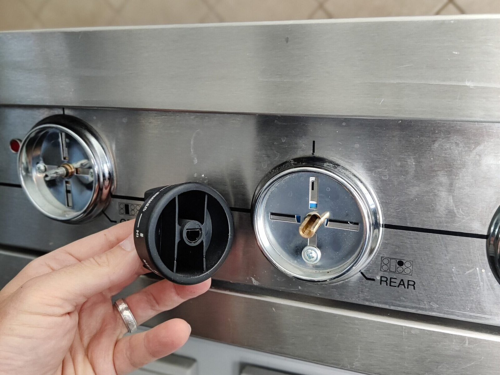 Close-up of a technician removing a control knob to access and repair the internal gas valves of a premium Wolf range.